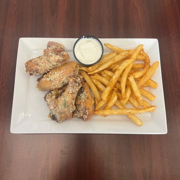 A white rectangular plate holds crispy fried chicken wings, golden french fries, and a small cup of white dipping sauce.