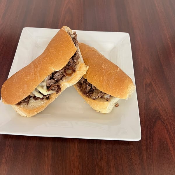 Two halves of a Philly cheesesteak sandwich with melted cheese and onions on a white plate.