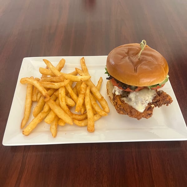 Crispy chicken sandwich with melted cheese, lettuce, and tomato, served with a side of golden french fries.