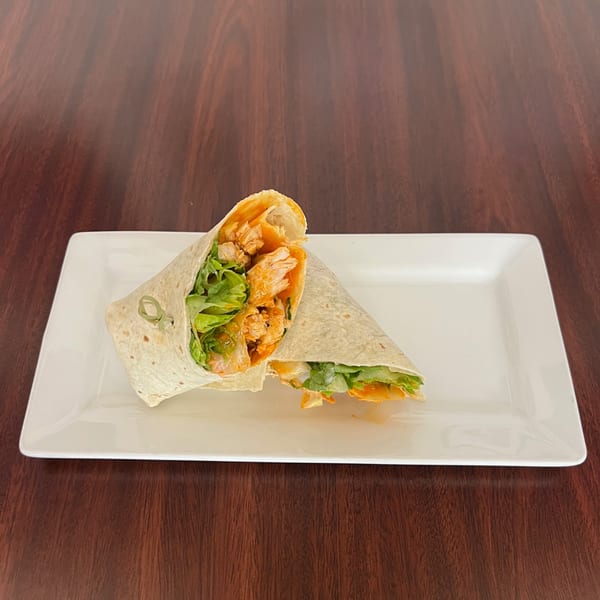 Two halves of a buffalo chicken wrap with lettuce on a white rectangular plate.