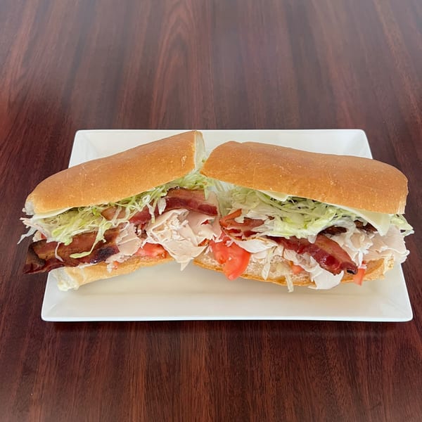 A large Peoples Choice Pizza sub sandwich, cut in half, filled with bacon, turkey, lettuce, and tomato.