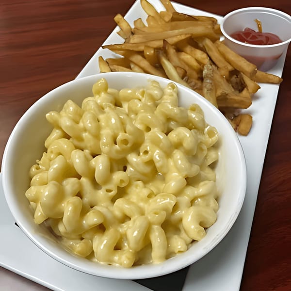 A white bowl of creamy macaroni and cheese next to a plate of golden french fries with ketchup.