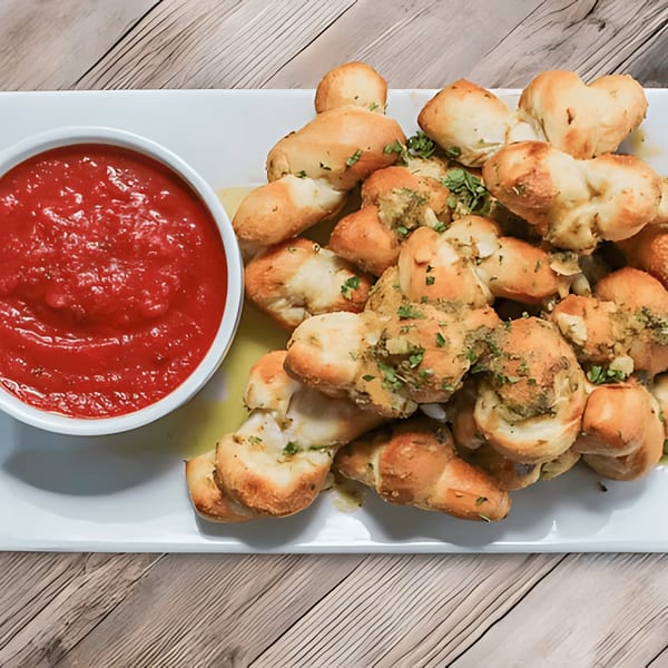 Peoples Choice Pizza garlic knots with herbs and a side of red marinara sauce.