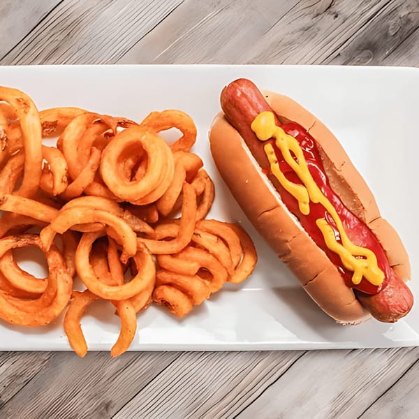 A hot dog with ketchup and mustard next to a pile of curly fries on a white plate.