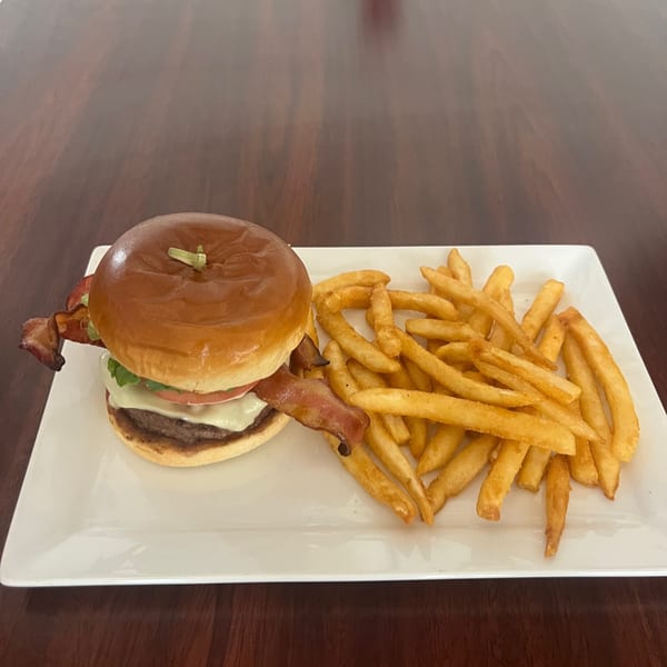 A bacon cheeseburger with lettuce and tomato next to a pile of golden french fries on a white plate.