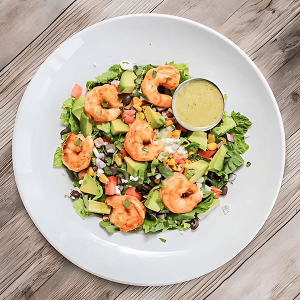 A vibrant shrimp salad with avocado, corn, black beans, and dressing on a white plate.