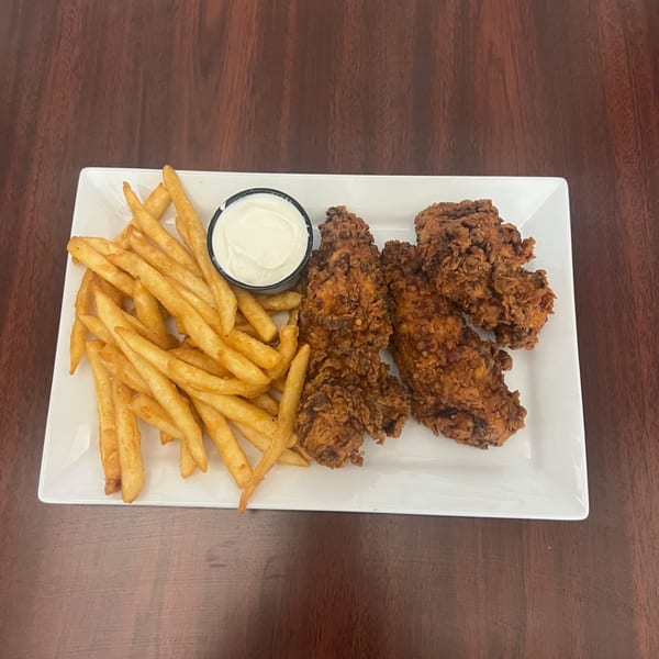 A white rectangular plate holds crispy fried chicken tenders, golden french fries, and a small cup of white dipping sauce.